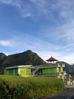 A green building with a red-roofed pavilion, surrounded by lush greenery and hills.