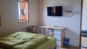 A bedroom with a bed, a desk, a chair, a television, and a window with curtains. - Surya Bromo Homestay (Ngadisari)