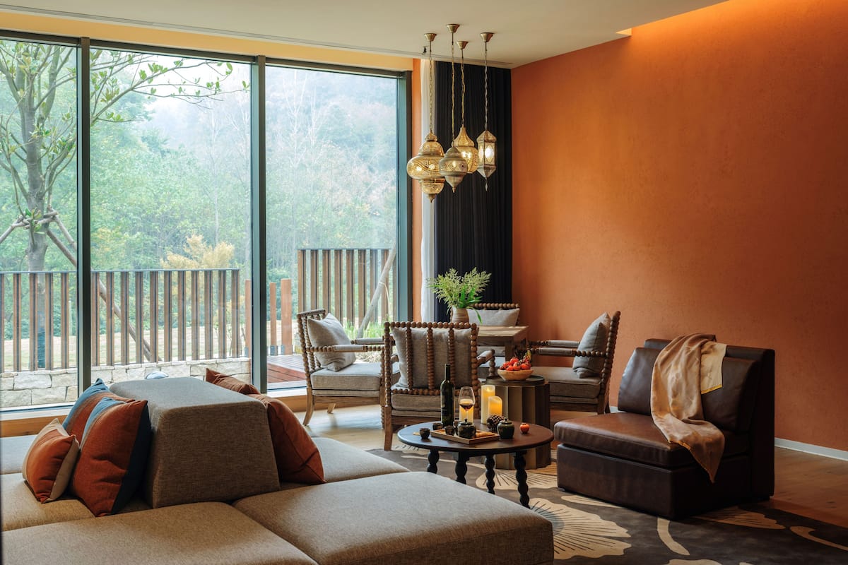 Una sala de estar moderna con un ventanal grande, un sofá, una mesa de centro con objetos decorativos y una chimenea.