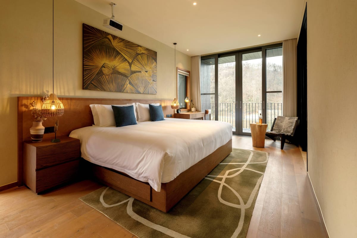 Habitación de hotel moderna con una cama grande, un escritorio, una silla y un balcón con vistas.