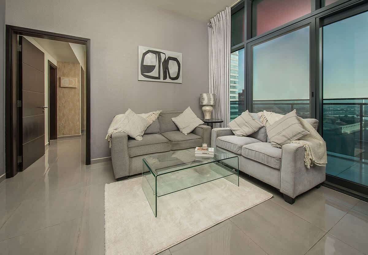 A modern living room with two sofas, a glass coffee table, and a large window offering a city view.