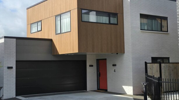 Una moderna casa a due piani con garage, una porta rossa e una parte in legno al piano superiore.