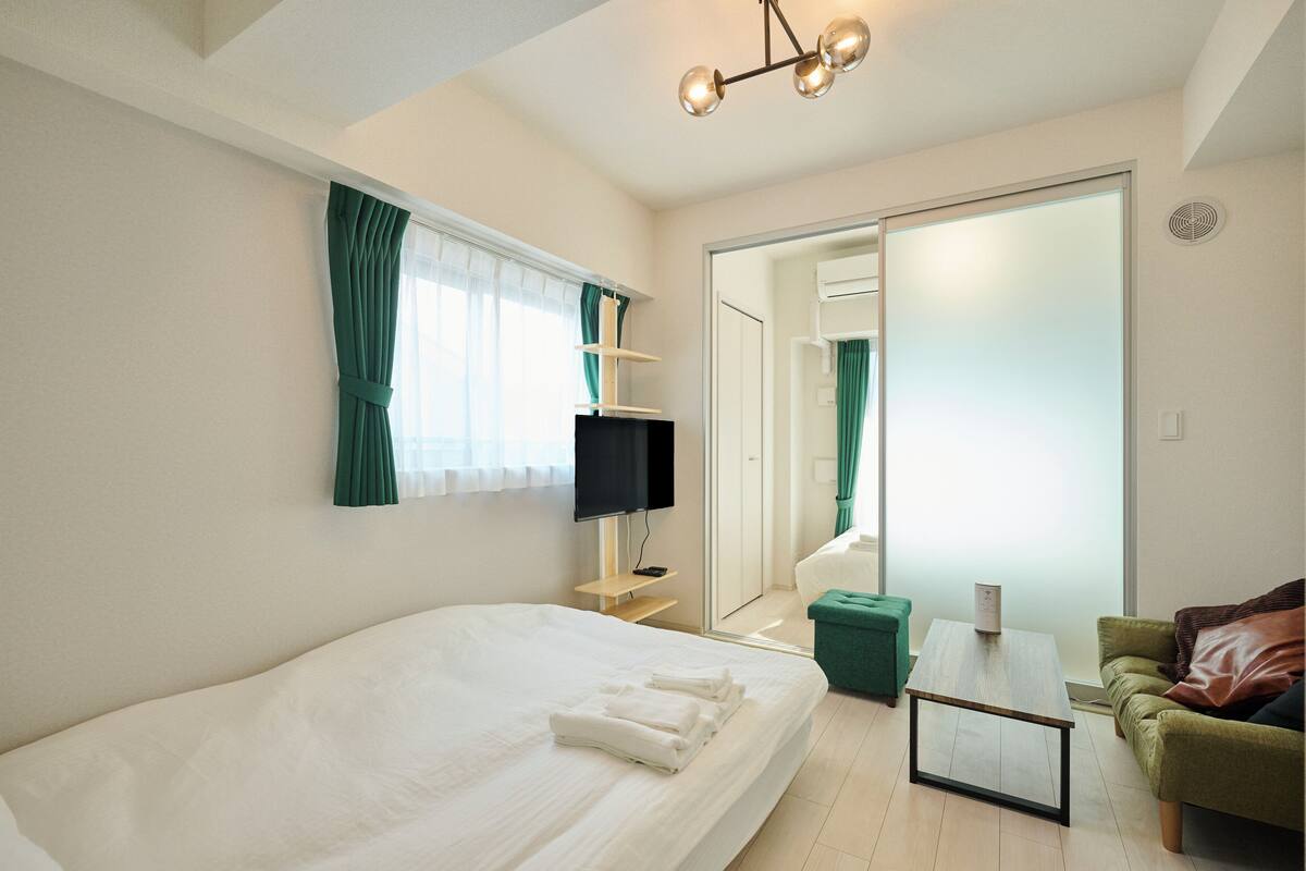 Een hotelkamer met een groot bed, een televisie, een kleine tafel, een groene stoel en een schuifdeur naar een andere kamer.