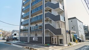 A multi-story building with balconies, a parking area, and a sign indicating a price range. - Gekkō Hakata Higashi (Fukuoka)