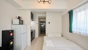 A compact hotel room with a kitchenette, a bed, and a view of the hallway.