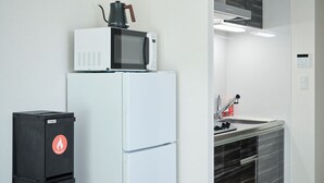 A compact kitchenette with a microwave, refrigerator, and a trash bin. - Gekkō Hakata Higashi (Fukuoka)