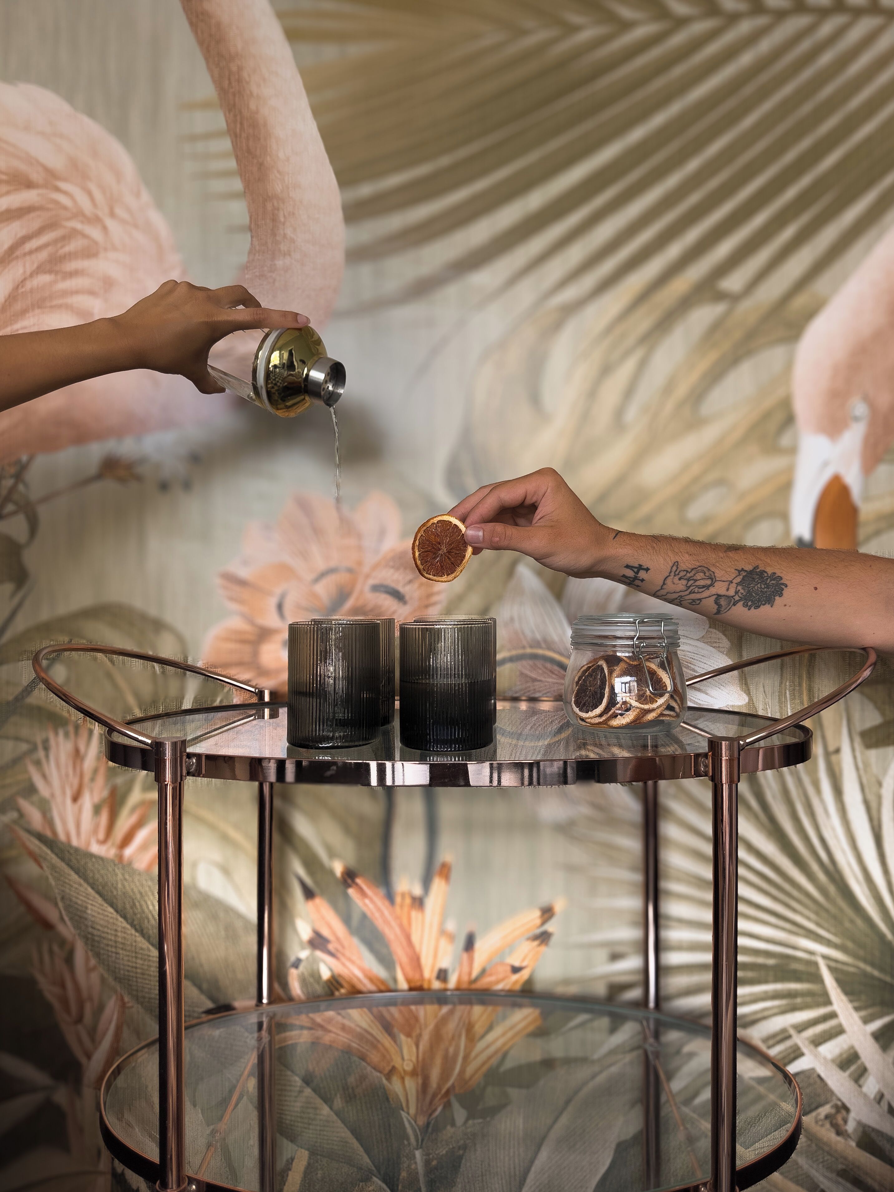 A person pouring a liquid from a bottle into a glass jar on a round table with a glass top.