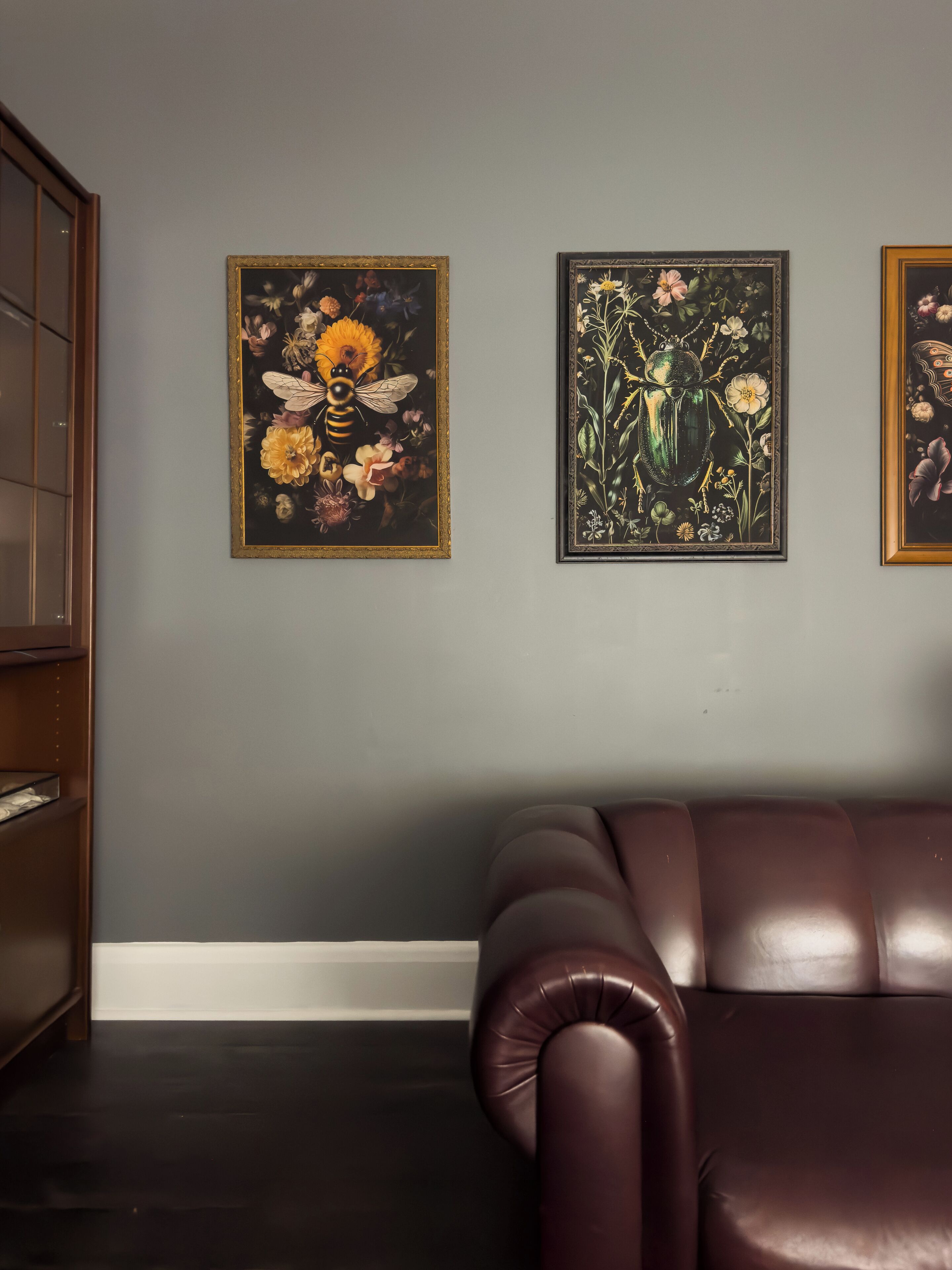 Une pièce avec un canapé en cuir marron, une commode et deux tableaux floraux encadrés accrochés au mur.
