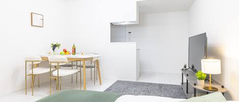 Een moderne hotelkamer met een bed, een bureau, een stoel, een televisietoestel en een klein tafeltje met fruit en een fles.