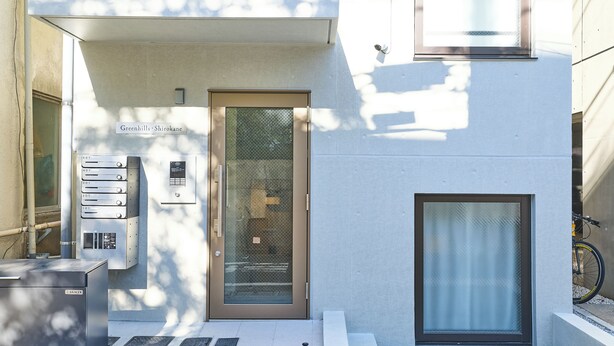 A modern building entrance with a glass door, a security keypad, and a bicycle parked nearby. - Greenhills Shirokane (Tokyo)