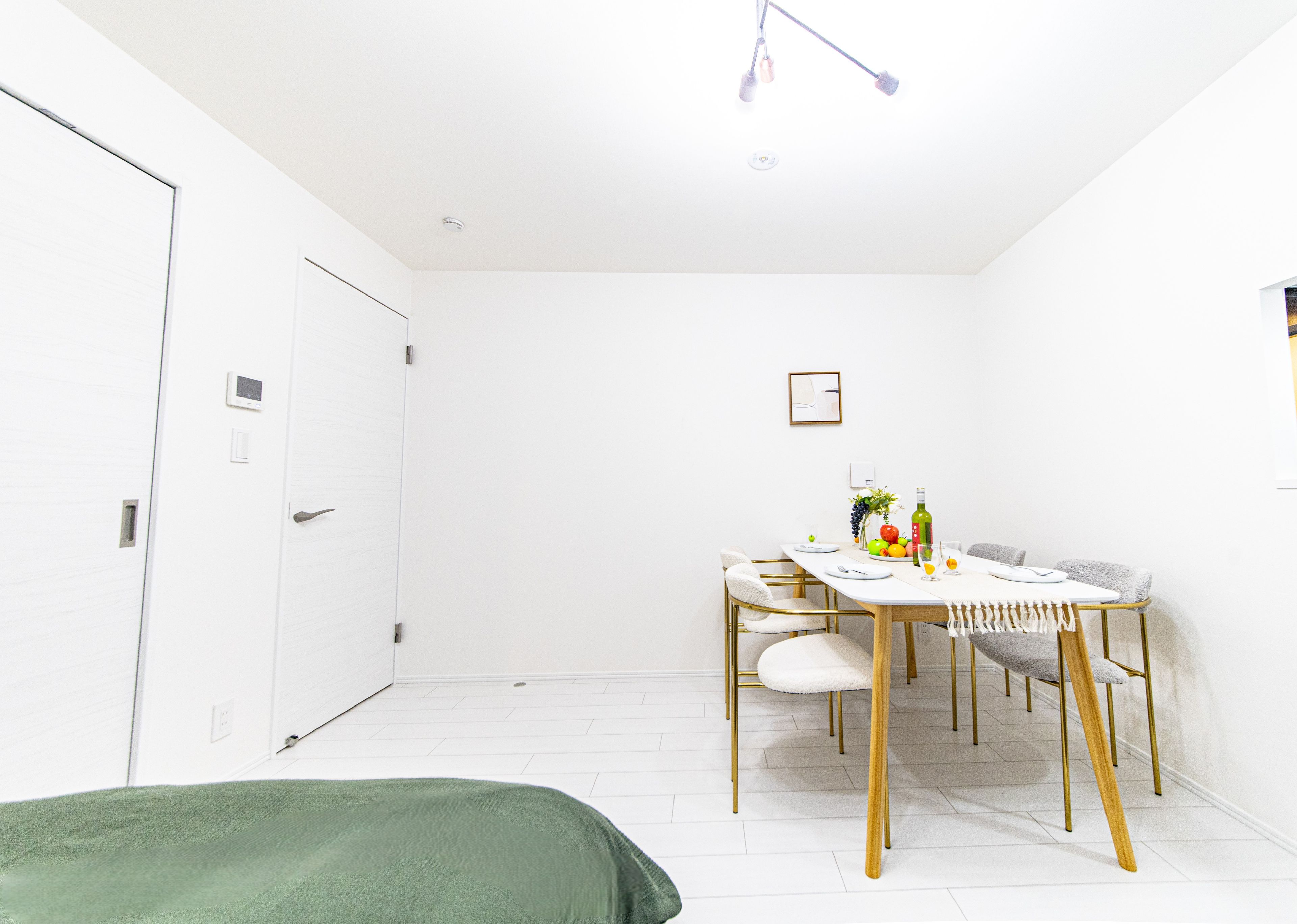 A minimalist room with a bed, a dining table with chairs, and a small kitchenette area.