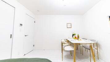 A minimalist room with a bed, a dining table with chairs, and a small kitchenette area.