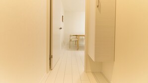 A narrow hallway with white walls and a tiled floor leading to a room with a bed and a chair. - Greenhills Shirokane (Tokyo)