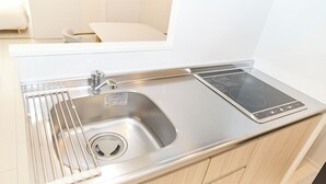 A modern kitchen with a stainless steel sink, a built-in stovetop, and light wooden cabinets. - Greenhills Shirokane (Tokyo)