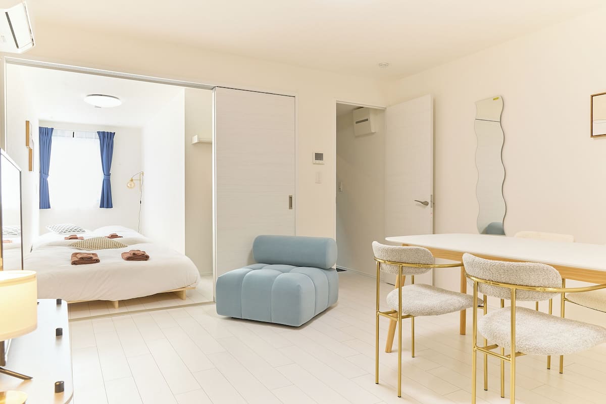Una habitación de hotel moderna con una cama, una zona de estar con mesa y sillas, y un espejo grande en la pared.