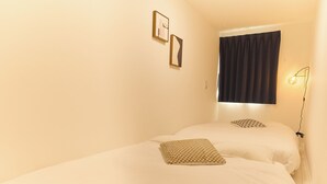 A room with two beds, a window with curtains, and a wall-mounted lamp. - Greenhills Shirokane (Tokyo)