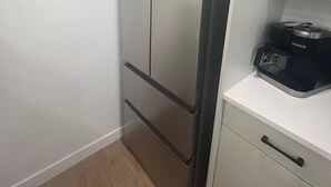 Et lille køkken med et rustfrit stål køleskab, en kaffemaskine på bordpladen og et hvidt skab.