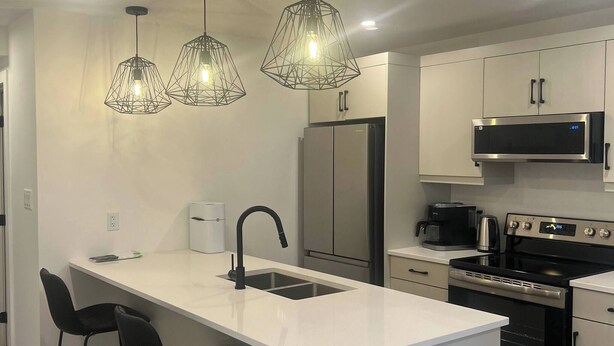 Et moderne køkken med en central ø, rustfrie hårde hvidevarer, hængende lamper og et minimalistisk design.
