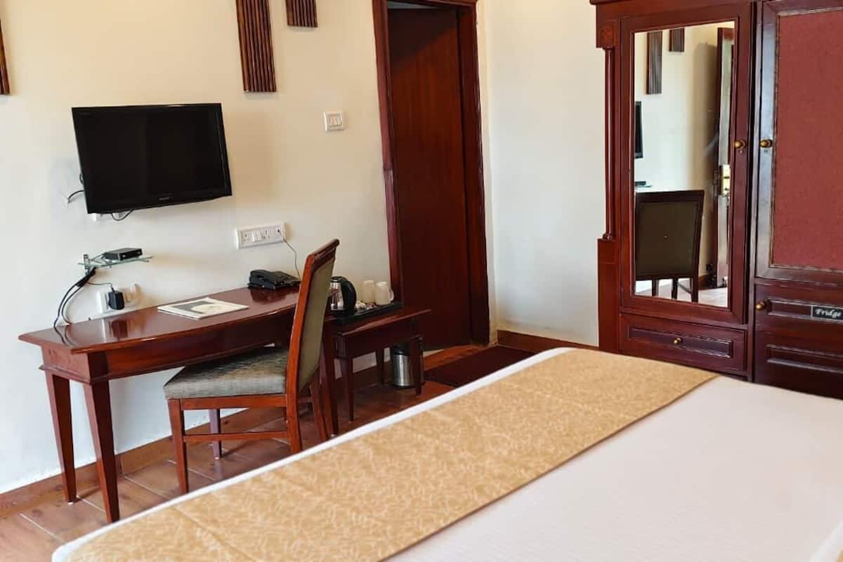 A hotel room with a bed, a desk with a chair, a television, and a wardrobe.