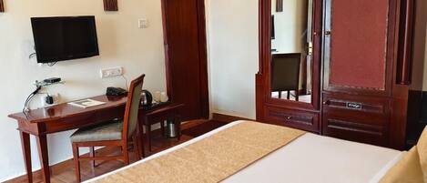 A hotel room with a bed, a desk with a chair, a television, and a wardrobe.