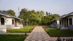 A pathway leading to two white buildings with balconies, surrounded by greenery and trees.
