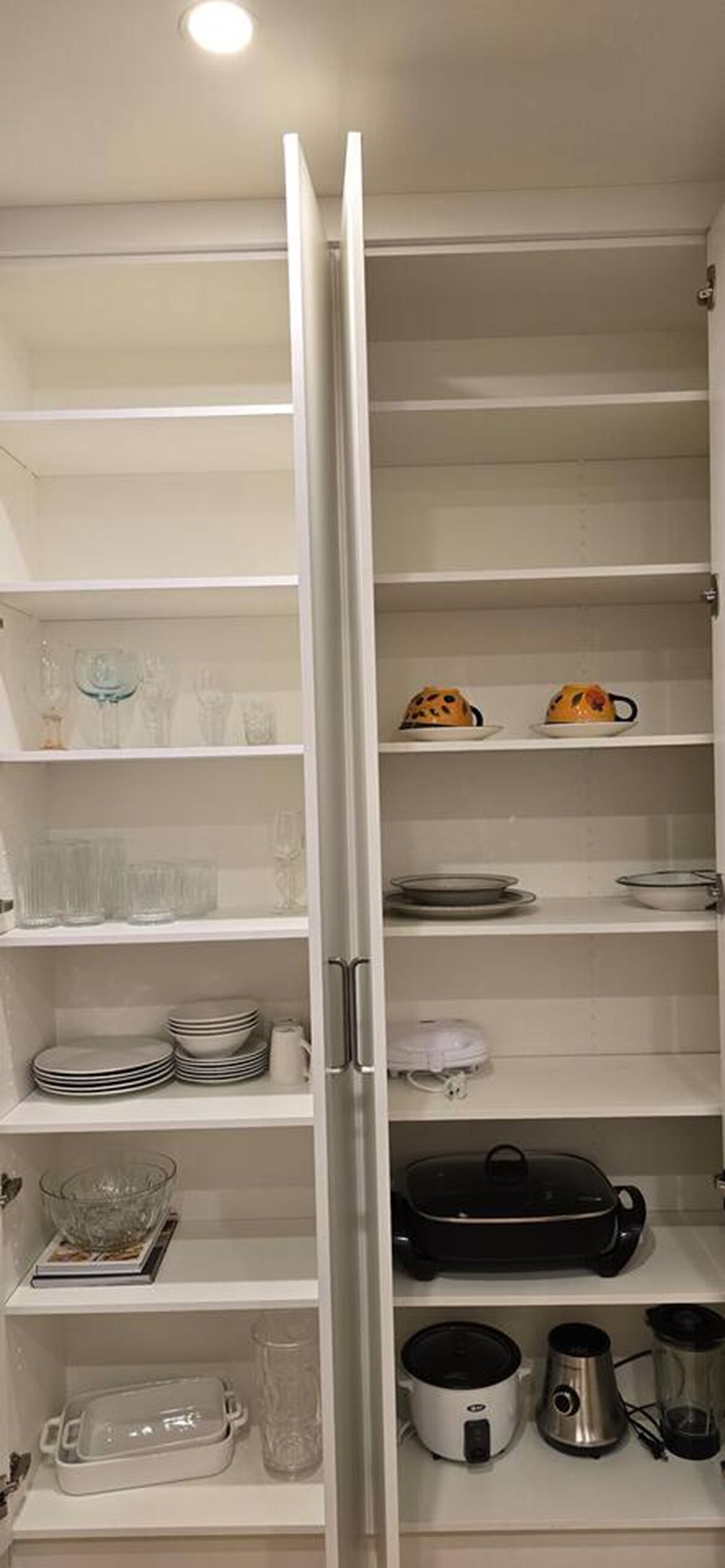 Et køkken med åbne skabe, der viser tallerkener, glas og hårde hvidevarer.