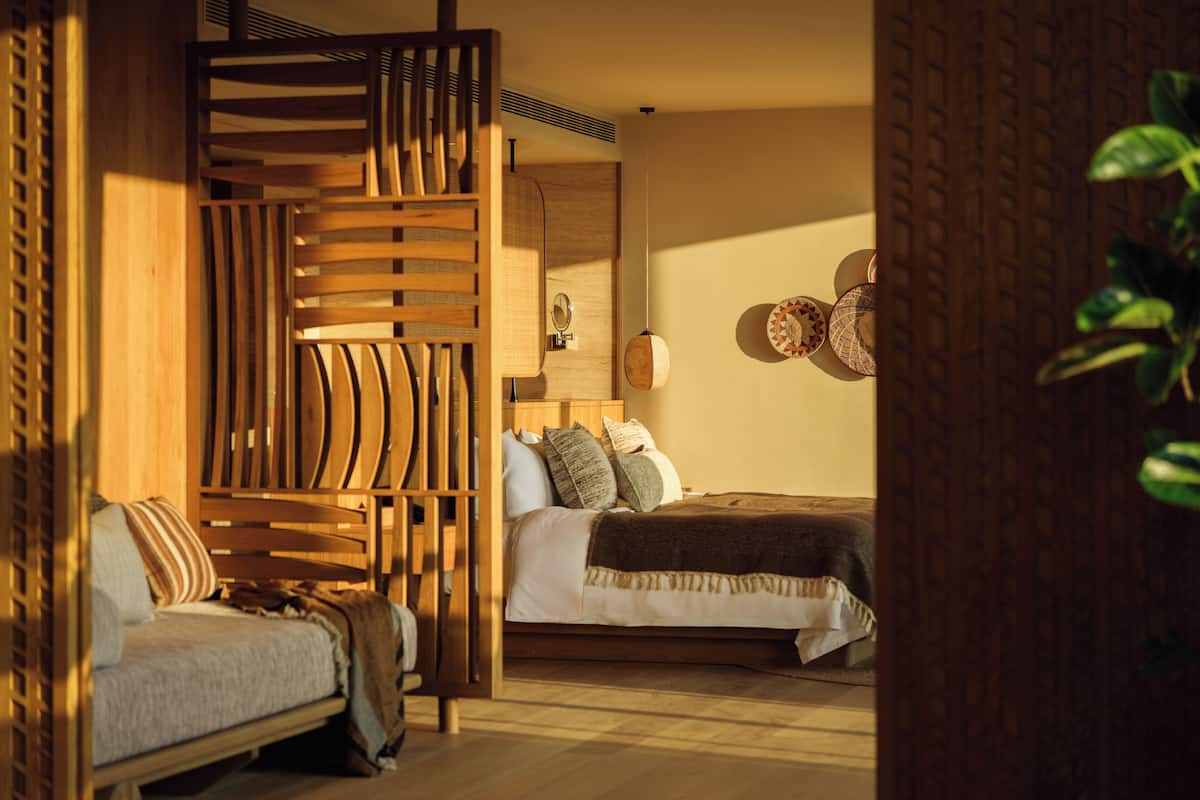 Een kamer met een bed, een bank, een houten scheidingswand en een wandlamp.