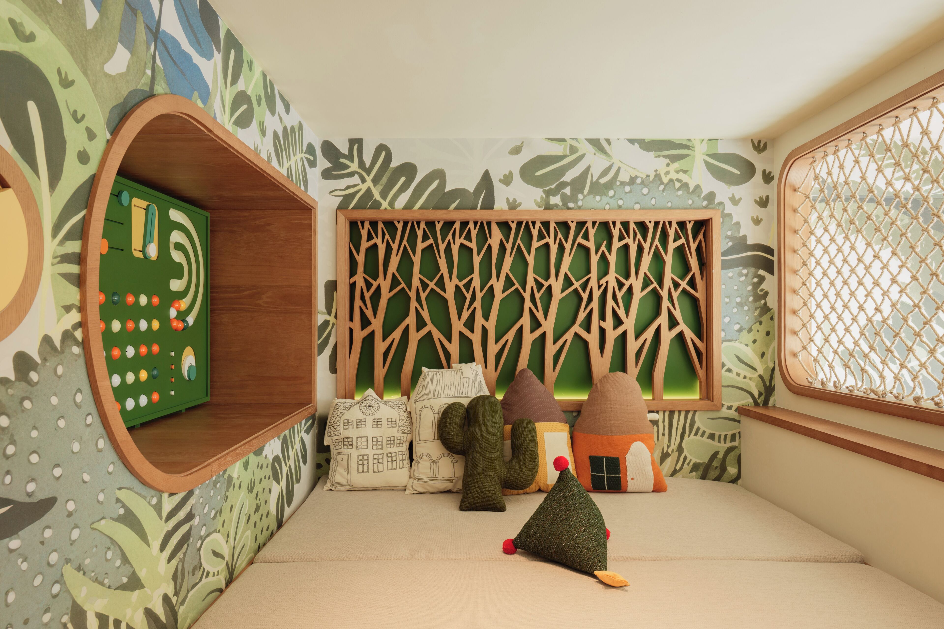 A children's playroom with a green board game, wooden houses, and a treehouse play structure.