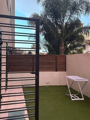 Ein durch eine Mauer abgeschirmter Patio-Bereich mit Kunstgr Rasen, einem klappbaren Metalltisch und einer großen Palme.