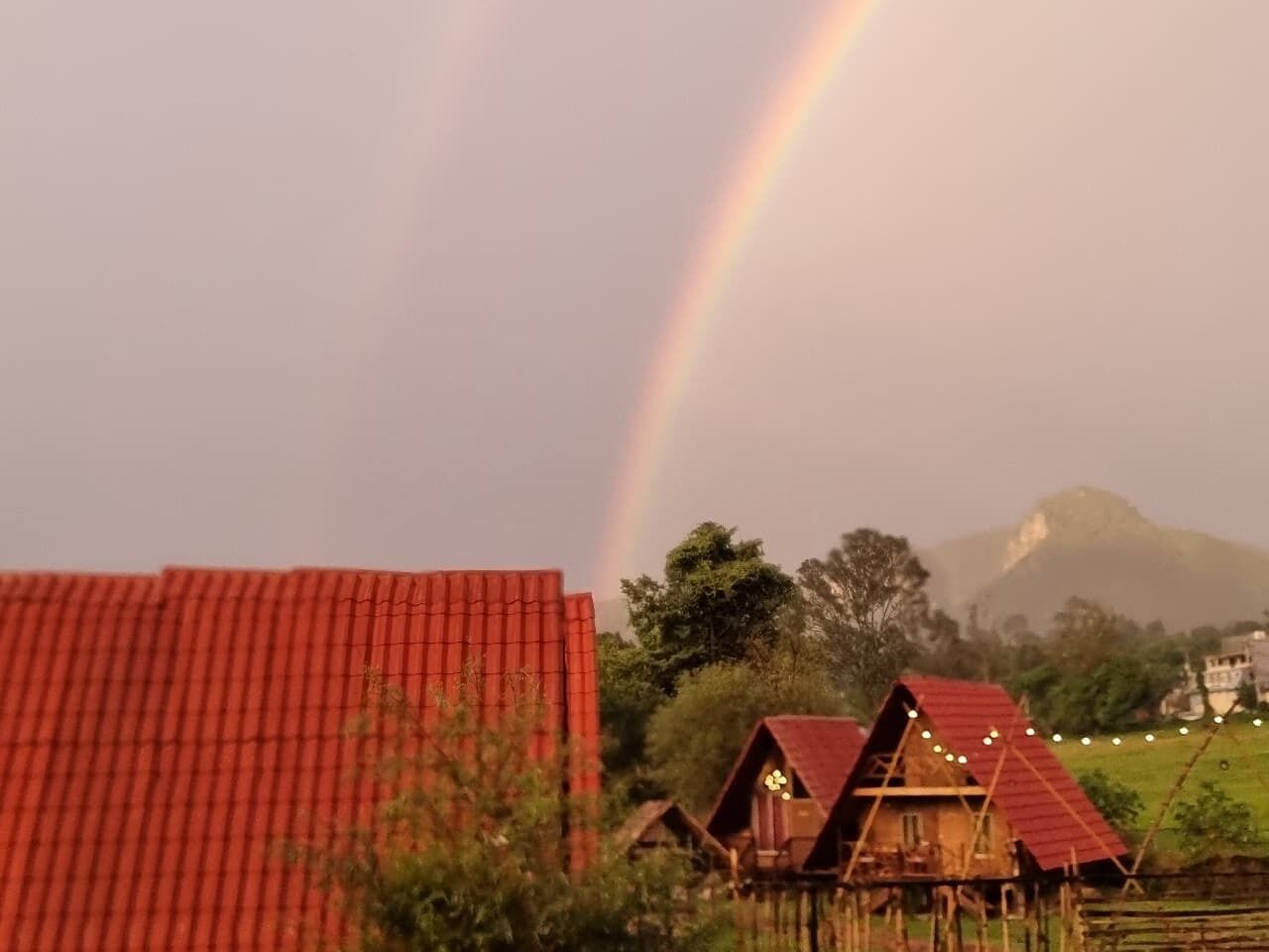 A rural landscape with a rainbow, a red-roofed barn, and traditional wooden houses.