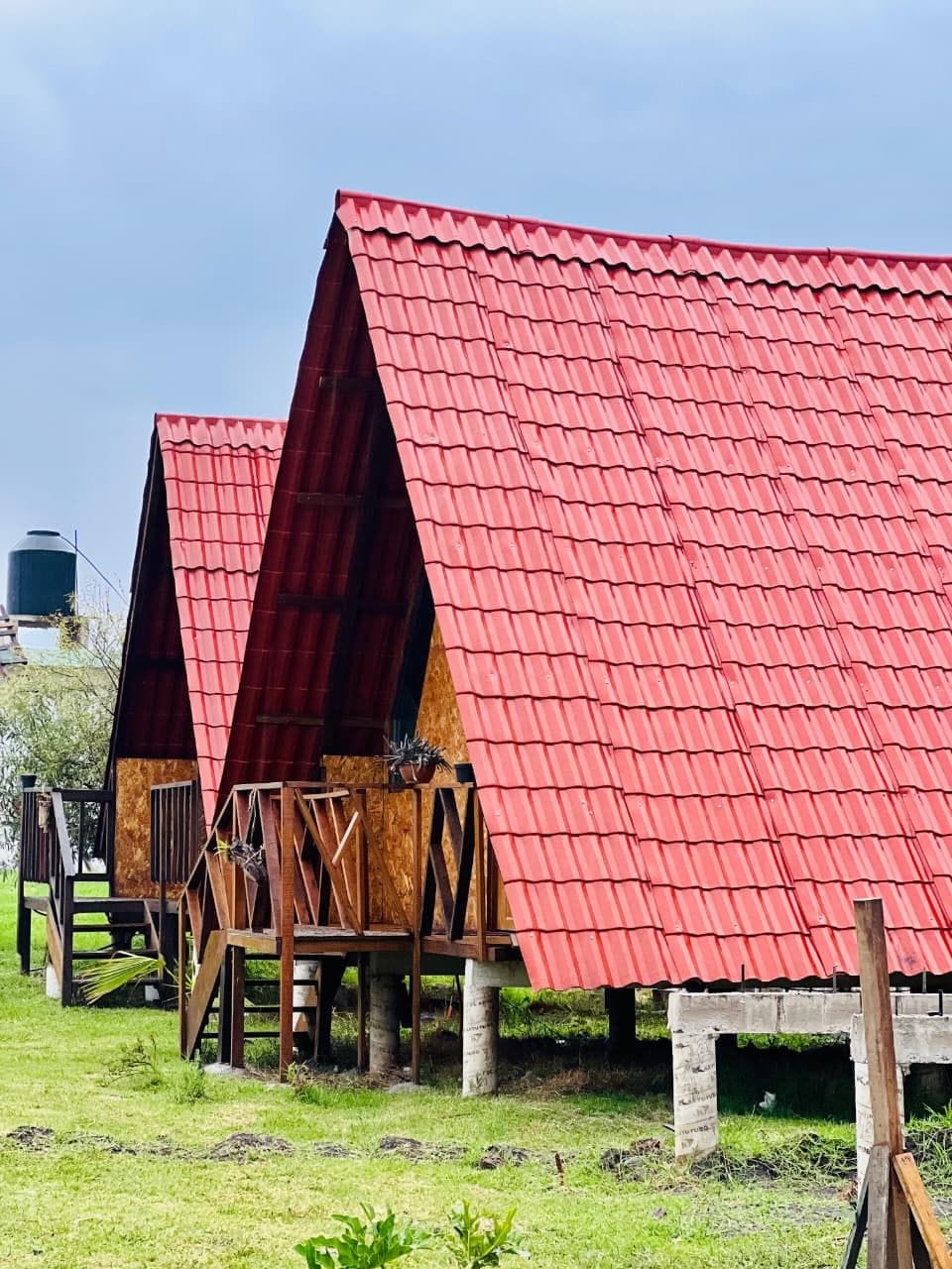 Filas de construcciones con techo rojo y soportes de madera, posiblemente una granja o alojamiento rural.