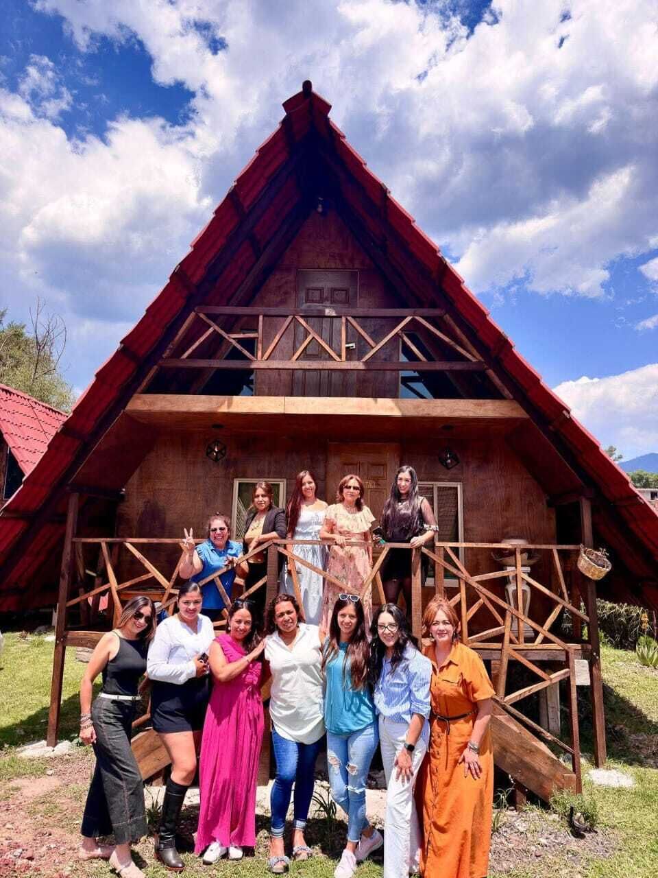 A group of people standing in front of a wooden cabin with a steep roof and a balcony.