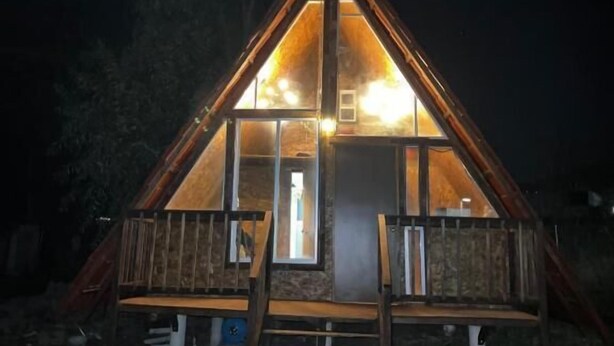 A wooden cabin with a triangular roof, large windows, and a wooden staircase leading to the entrance. - Hospedaje Valle Colibrí (Tuxpan)