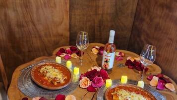 Una mesa de madera con dos platos de comida, velas y una botella de licor.