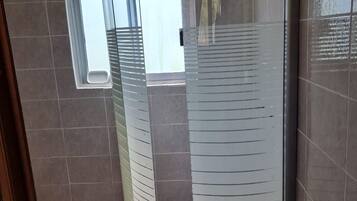A glass-enclosed shower with a curved design, a window above it, and tiled walls.