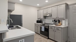 A modern kitchen with grey cabinets, stainless steel appliances, and a white countertop.