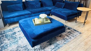 A blue sectional sofa with a matching ottoman, a small round table, and a tray with candles and flowers.