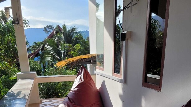 A balcony with a table and chairs, a view of greenery and mountains, and a tiled floor. - White lotus house (Maret)