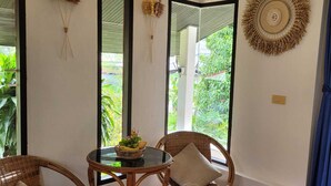 A room with a dining table, two wicker chairs, a mirror, and a decorative wall piece. - White lotus house (Maret)