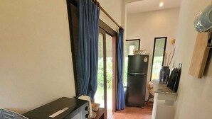 A compact kitchen with a microwave, toaster, and a refrigerator. There is a window with curtains, and a small dining area with a chair. - White lotus house (Maret)