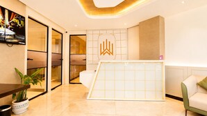 A modern hotel lobby with a reception desk, a seating area, and a large window. - White Wharf Manesar (Gurugram)