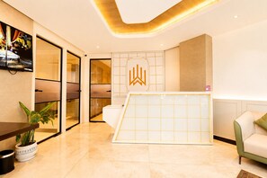 A modern hotel lobby with a reception desk, a seating area, and a large window.