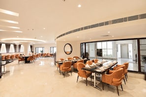 A spacious dining area with round tables and orange chairs, a large mirror on the wall, and a view of the outside through large windows. - White Wharf Manesar (Gurugram)