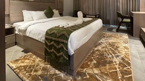 A modern hotel room with a large bed, a ceiling fan, a desk, and a view of the city. - White Wharf Manesar (Gurugram)