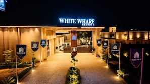 The entrance to White Wharf Resort with a well-lit pathway, a reception area, and multiple flags. - White Wharf Manesar (Gurugram)