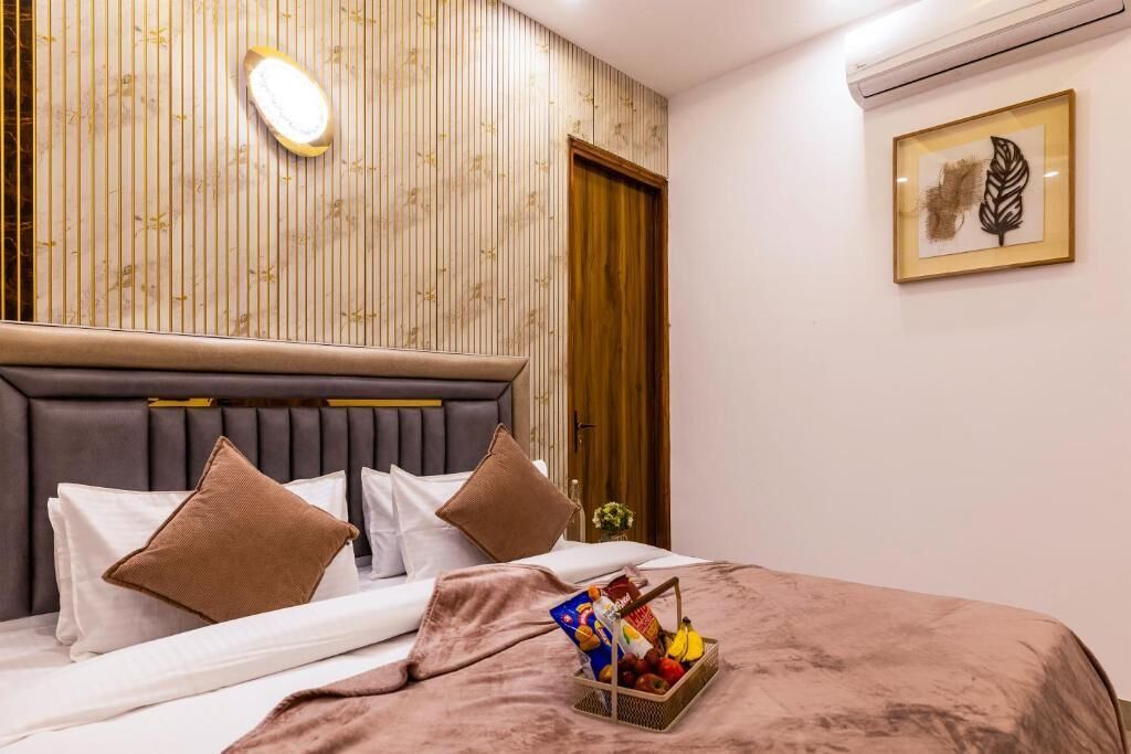 Un lit bien fait, avec une couverture marron et un panier de fruits, un mur recouvert de panneaux en bois, une œuvre d’art encadrée et une porte en bois.