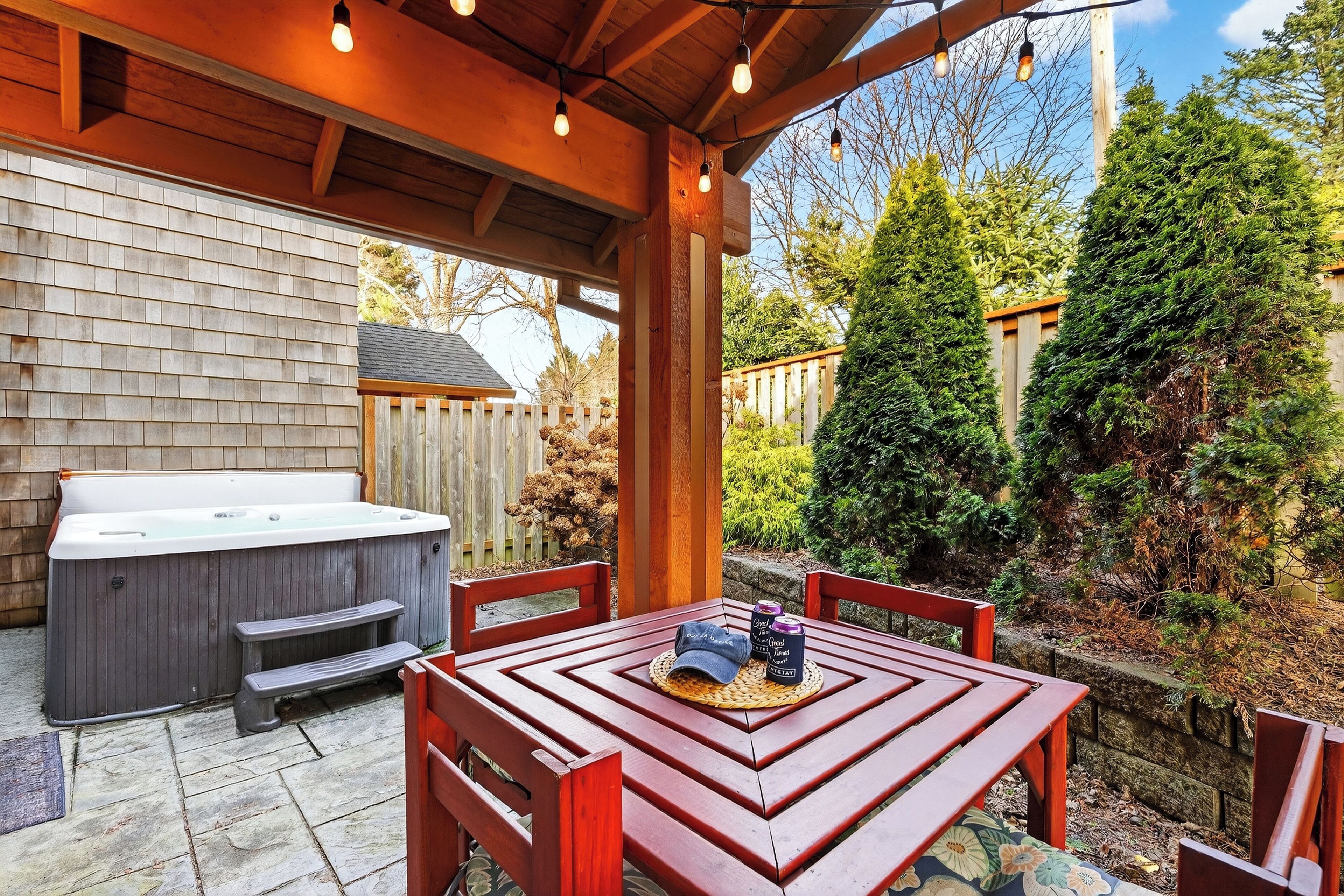 A wooden deck with a hot tub, a table with chairs, and a pergola with string lights.