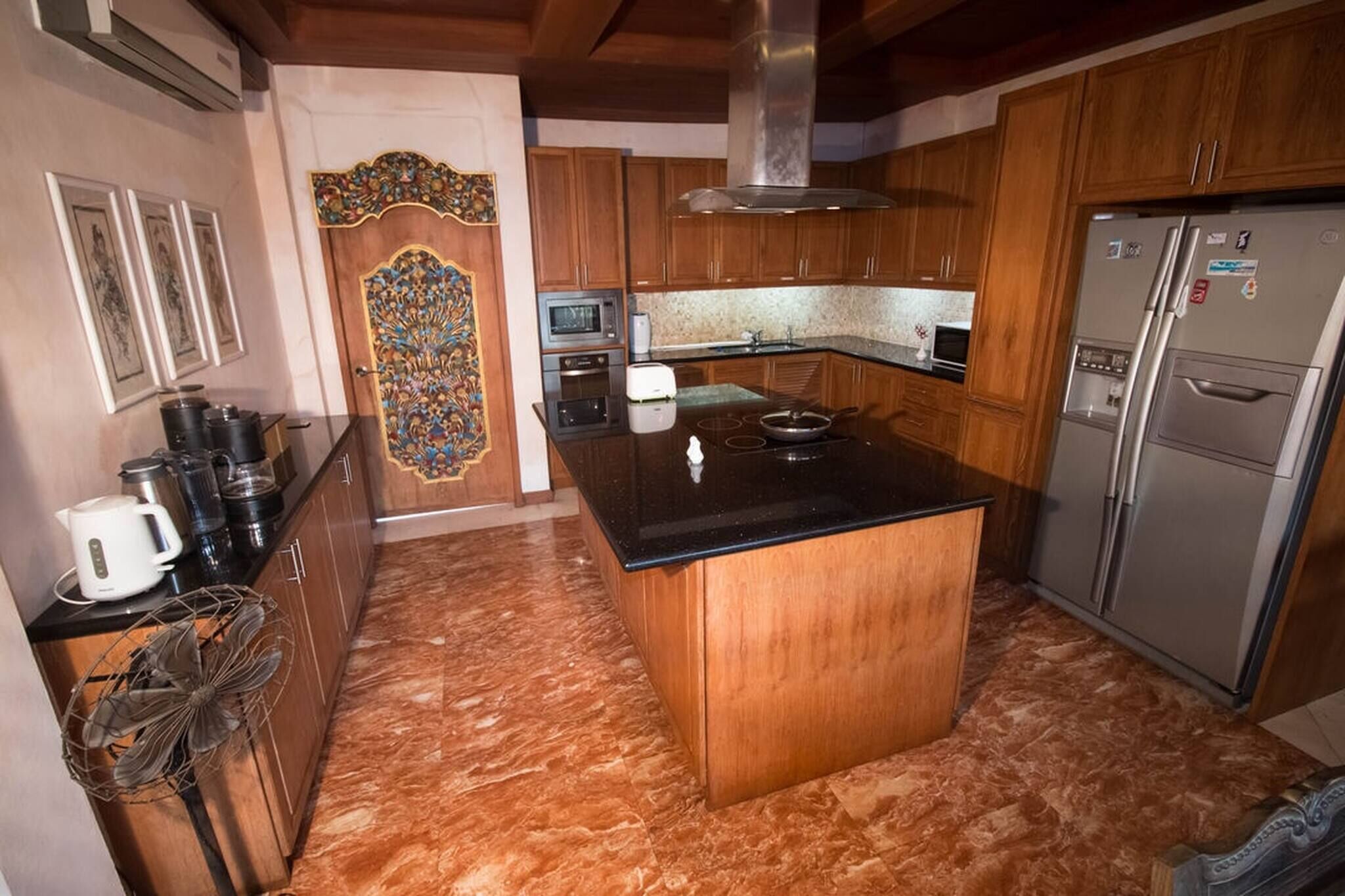 A kitchen with wooden cabinets, a central island, a stainless steel refrigerator, and a microwave.