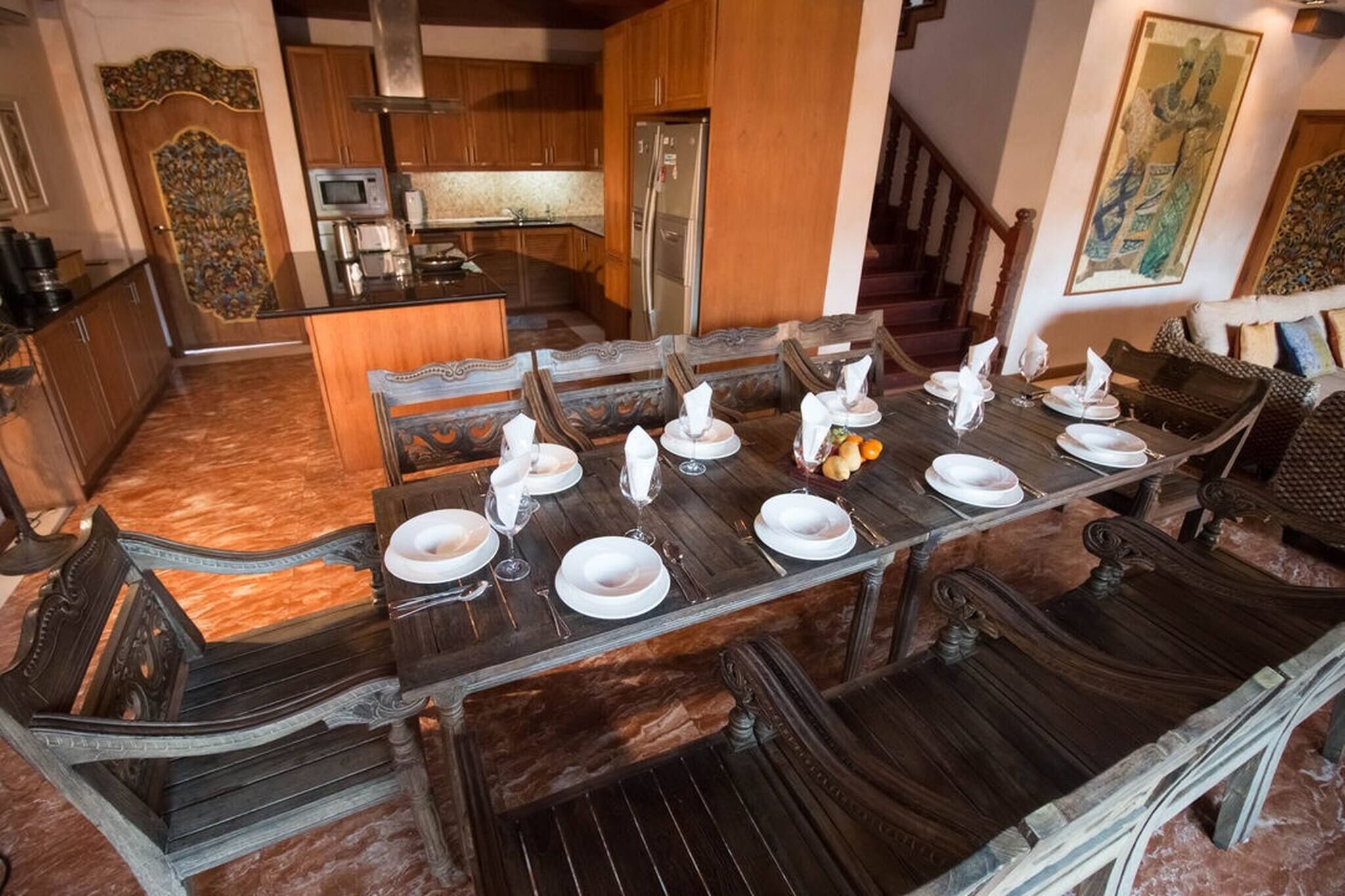 A dining area with a long wooden table set for six, surrounded by ornate chairs.