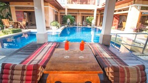A poolside area with a wooden table, two cushioned seats, and two glasses of red drink. - Exclusive Balinese Pool Villa in Pattaya (Pattaya)
